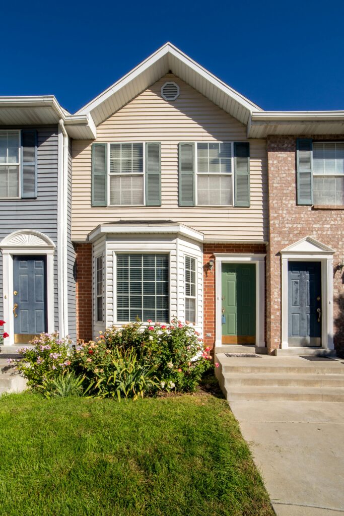 Front view of a suburban townhouse with well-maintained lawn and blue sky.